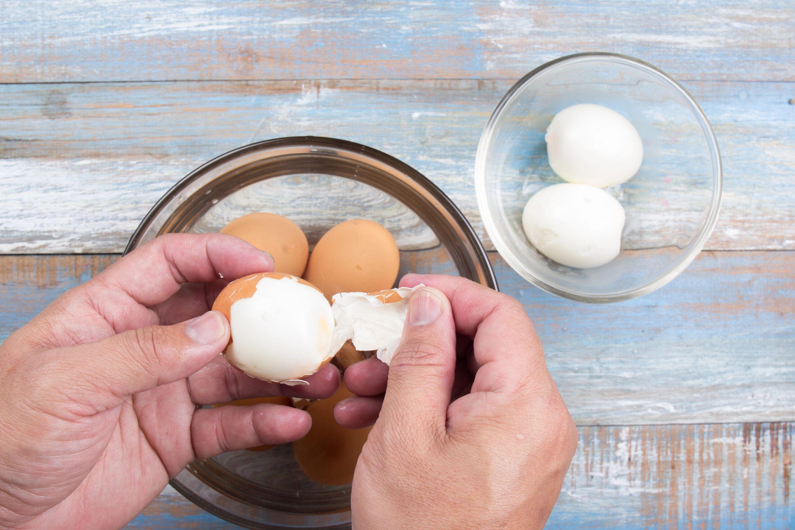 A person's hands peeling the shell off a hard-boiled egg easily after using the boiling method.