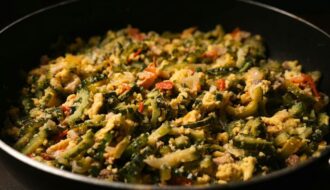 A pan of stir-fried bitter melon with scrambled eggs, tomatoes, onions, and garlic